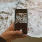 Ръка държи телефон с плажна снимка в Instagram, докато седи на плажа