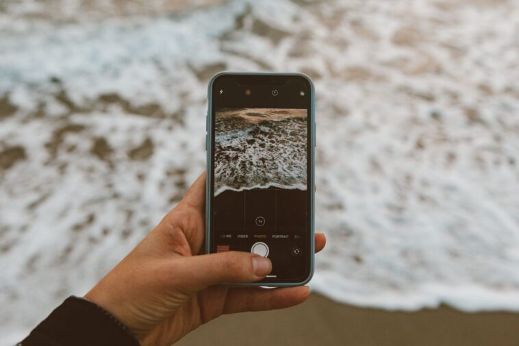 Ръка държи телефон с плажна снимка в Instagram, докато седи на плажа