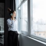 Жена гледа замислено през прозорец на офис през есента