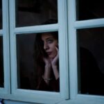 Жена гледа през прозореца през зимата, усещане за самота