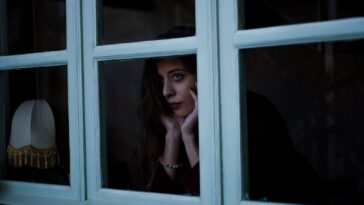 Жена гледа през прозореца през зимата, усещане за самота